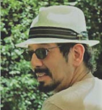 headshot of a man with dark hair, sunglasses and hat, looking left